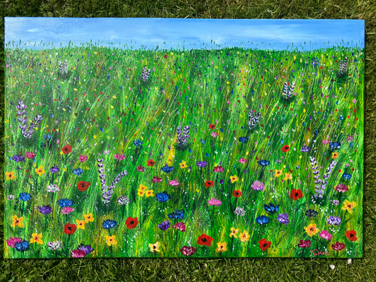 A photo of an original acrylic painting of a meadow of bright colourful flowers. There is a thin strip of blue sky at the top of the painting and the rest is green grass with some yellow strands and different types of pink, blue, purple, yellow and red flowers. The painting is signed KtKell in the bottom right hand side.
