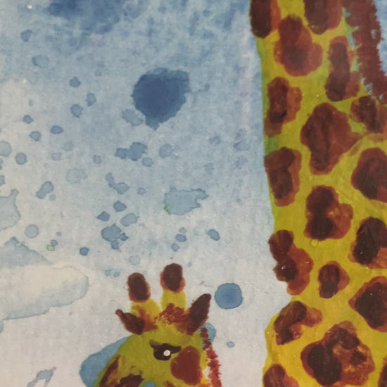 A photo of an original watercolour of a parent giraffe, either mother or father with a baby giraffe looking up at them with a blue splattered background. The painting is in a white frame on a mantlepiece.